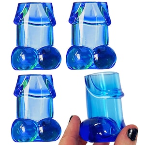 May include: Set of four blue shot glasses shaped like a male anatomy. The glasses are made of clear plastic and have a shiny finish.