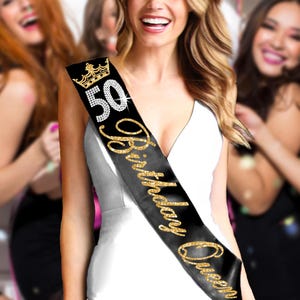 May include: Black satin sash with gold glitter text that reads "50 Birthday Queen". A gold crown with rhinestones is above the number 50. The sash is worn diagonally across the chest.