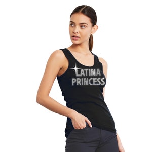 May include: A black sleeveless tank top featuring the text LATINA PRINCESS in a silver-toned, rhinestone-style font across the chest, accompanied by a small four-pointed star graphic positioned above the first letter of the word LATINA.