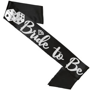 以下が含まれることがあります： 「Bride to Be」の文字とダイヤモンドのグラフィックが施された、黒いサテンのサッシュ。左上にはハートとドットの模様が入った白いサイコロが2つあります。ブライダルのお祝いにぴったりの楽しいアクセサリーです。
