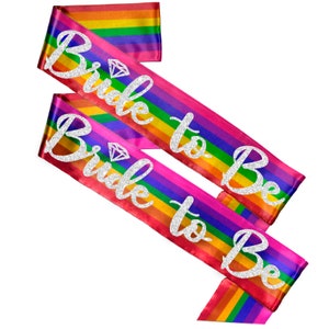 May include: Two rainbow satin sashes with silver glitter text that reads "Bride to Be" and a diamond symbol.