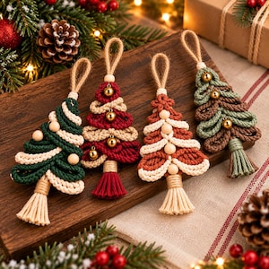 Peut inclure: Quatre décorations de Noël en macramé en forme de sapin, faites de corde de coton torsadée vert foncé, rouge, rouille et vert sauge. Chaque sapin présente des couches alternées de corde crème, des perles en bois et des grelots dorés.