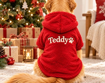 Può includere: Un maglione con cappuccio in pile rosso brillante per cane, con il nome Teddy e una grafica a forma di zampa ricamata in bianco sul retro. Il capo è realizzato in materiale morbido e testurizzato, pensato per un cane, visto da dietro.