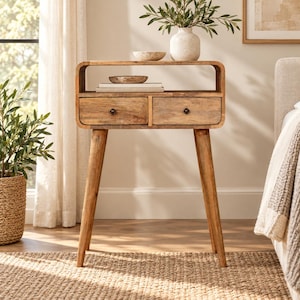 May include: A light brown wooden console table featuring a rectangular top with rounded corners, an open storage shelf, and two drawers with small dark knobs. The table is supported by four tapered legs and has a visible natural wood grain finish.