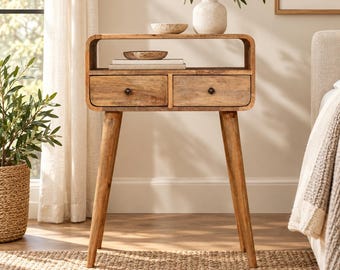 May include: A light brown wooden console table featuring a rectangular top with rounded corners, an open storage shelf, and two drawers with small dark knobs. The table is supported by four tapered legs and has a visible natural wood grain finish.