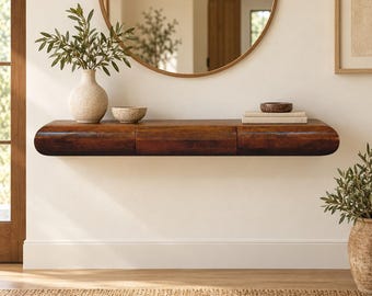 May include: A dark brown wooden floating console table with rounded edges and a smooth finish. The table is mounted on a wall and features a long, horizontal design with a seamless front panel, providing a surface for decorative items.