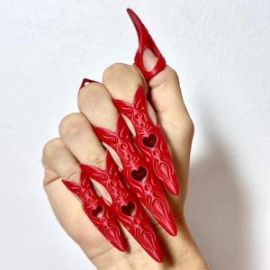 May include: A set of five red, pointed finger armor pieces worn on the fingers. Each piece features an elongated, tapered shape with intricate embossed patterns and a small heart-shaped cutout in the center, covering the fingernail area.