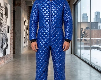 Può includere: Una tuta intera trapuntata blu brillante con finitura lucida, chiusura frontale con zip e cappuccio integrato. Il capo presenta maniche lunghe con polsini neri a coste, un motivo a losanghe su tutta la superficie e gambe lunghe.