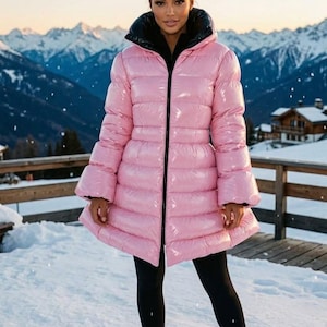 Può includere: Un piumino rosa chiaro lucido con collo alto, maniche lunghe e orlo svasato. La giacca presenta una chiusura frontale con zip nera e una fodera interna nera, abbinata a leggings neri e stivali invernali stringati.