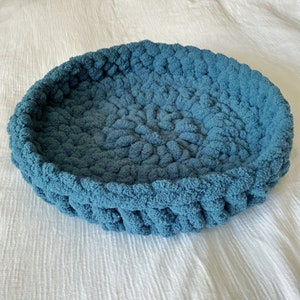 May include: A teal blue crocheted pet bed with a round shape and a textured surface.