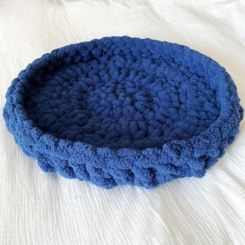 May include: A blue knitted pet bed with a round shape and a soft, fluffy texture.