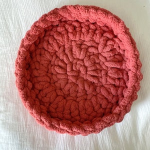 May include: A round, red crocheted pet bed with a textured surface.