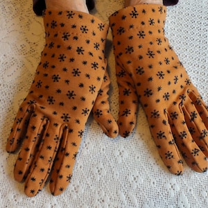Könnte beinhalten: Ein Paar braune Handschuhe mit einem schwarzen Schneeflockenmuster. Die Handschuhe sind aus einem weichen, strukturierten Stoff.