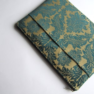 Könnte beinhalten: Eine Laptoptasche mit goldfarbenem und blaugrünem Muster und Reißverschluss.