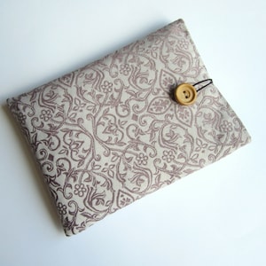 May include: A beige fabric pouch with a brown button closure and a brown and white floral pattern.