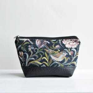 Könnte beinhalten: Eine schwarze Reißverschlusstasche mit einem floralen Tapisserie-Design mit Vögeln und Blumen. Die Tasche hat einen schwarzen Lederboden.