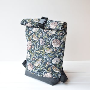Könnte beinhalten: Ein schwarzer Rolltop-Rucksack mit einem floralen Tapisserie-Design mit Vögeln und Blumen. Der Rucksack hat einen schwarzen Schnallenverschluss und verstellbare Träger.