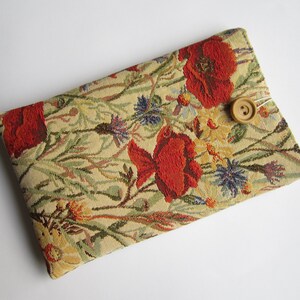 May include: A beige fabric pouch with a floral pattern featuring red poppies and blue wildflowers. A brown button is sewn onto the pouch.