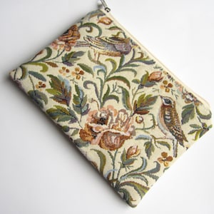 Könnte beinhalten: Eine beige Reißverschlusstasche mit einem floralen Tapisserie-Design mit Vögeln und Blumen in Braun-, Grün- und Rosatönen.
