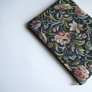 Puede incluir: Una bolsa negra con cremallera con un diseño de tapicería floral que presenta pájaros, flores y hojas en tonos de rosa, verde y azul.