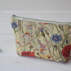Pu&ograve; includere: Una pochette beige con cerniera con un motivo di arazzo floreale con papaveri rossi, fiordalisi blu e foglie verdi.