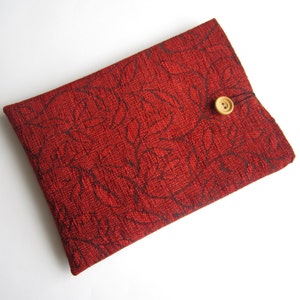 Op de afbeelding: Een rode stoffen tas met een bloemenpatroon en een houten knoopsluiting.