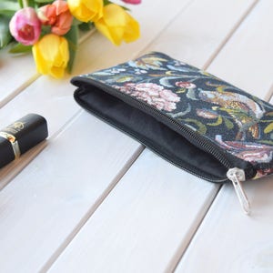 May include: A black zippered pouch with a floral tapestry design. The pouch is open and the lining is black.