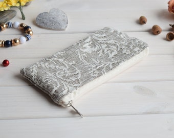 Puede incluir: Una pequeña bolsa con cremallera de color gris y blanco con un tirador de cremallera plateado. La bolsa está sobre una superficie de madera blanca.