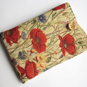 May include: A beige fabric pouch with a floral pattern featuring red poppies and blue flowers. The pouch has a wooden button closure.