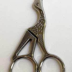 May include: Silver-toned bird-shaped scissors with a detailed design. The scissors have two circular handles.