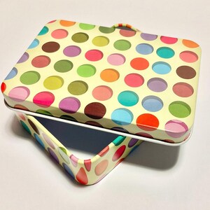 May include: A yellow tin box with a colourful polka dot pattern. The lid is open and the box is empty.