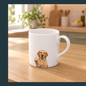 May include: A white ceramic mug featuring a graphic of a golden-coloured dog with a serious expression, depicted with one paw raised and a middle finger extended. The mug has a smooth, cylindrical body and a curved handle on the right side.