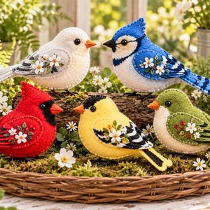 Peut inclure: Quatre oiseaux décoratifs en feutrine faits à la main, comprenant un oiseau blanc, un geai bleu, un cardinal rouge et un chardonneret jaune. Chaque oiseau est orné de fleurs blanches brodées et de feuilles vertes sur l'aile.