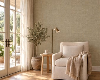 May include: An upholstered armchair with a beige throw blanket and a matching lumbar pillow. Beside the chair is a small wooden side table holding a white mug, a tall brass floor lamp, and a potted olive tree in a textured clay pot.