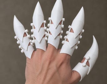 Op de afbeelding: Een set van vijf witte, gearticuleerde vingerharnasstukken met puntige, klauwachtige uiteinden. Elk stuk heeft een gesegmenteerd ontwerp dat is verbonden door kleine cilindrische scharnieren, die de lengte van de vingers bedekken voor een scherpe uitstraling.