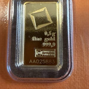 May include: A rectangular 0.5g fine gold 999.9 bullion bar encased in a clear protective plastic sleeve. The gold bar features a diamond-shaped logo, the text 0.5g fine gold 999.9, a CHI FONDEUR logo, and the serial number AA025883 printed on the surface.