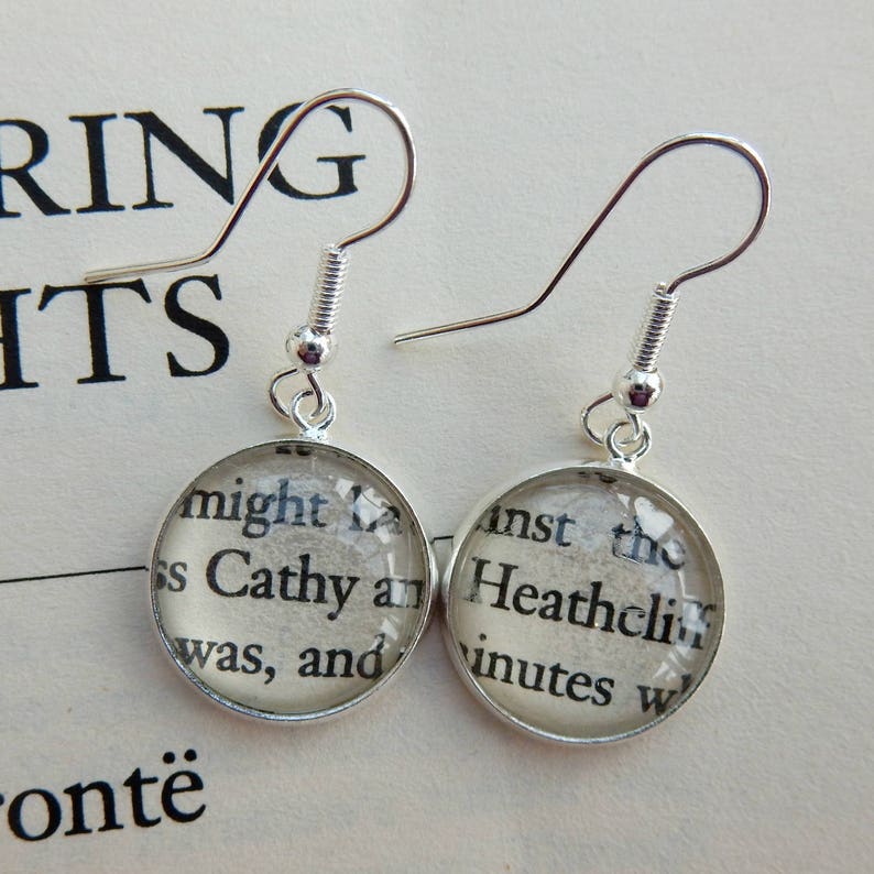 May include: Silver earrings with round glass charms featuring text from the book "Wuthering Heights" by Emily Bront&euml;. The text on the charms reads "might L ss Cathy and was, and" and "inst the Heathclif inutes W".