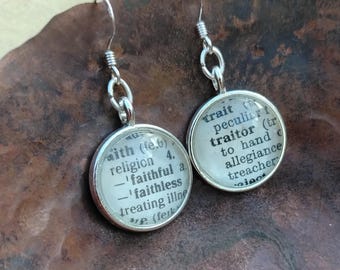 May include: A pair of silver-toned drop earrings featuring circular pendants. Each pendant contains a small piece of paper printed with dictionary definitions, including the words faith, faithful, faithless, trait, and traitor, under a clear glass dome.