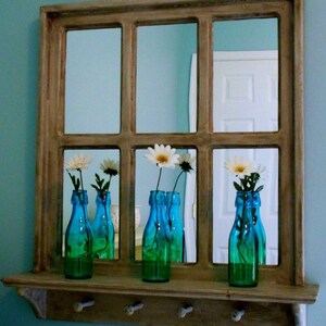 May include: A wooden framed mirror with a shelf and hooks underneath. The mirror is divided into nine panes and reflects white flowers in blue glass bottles.