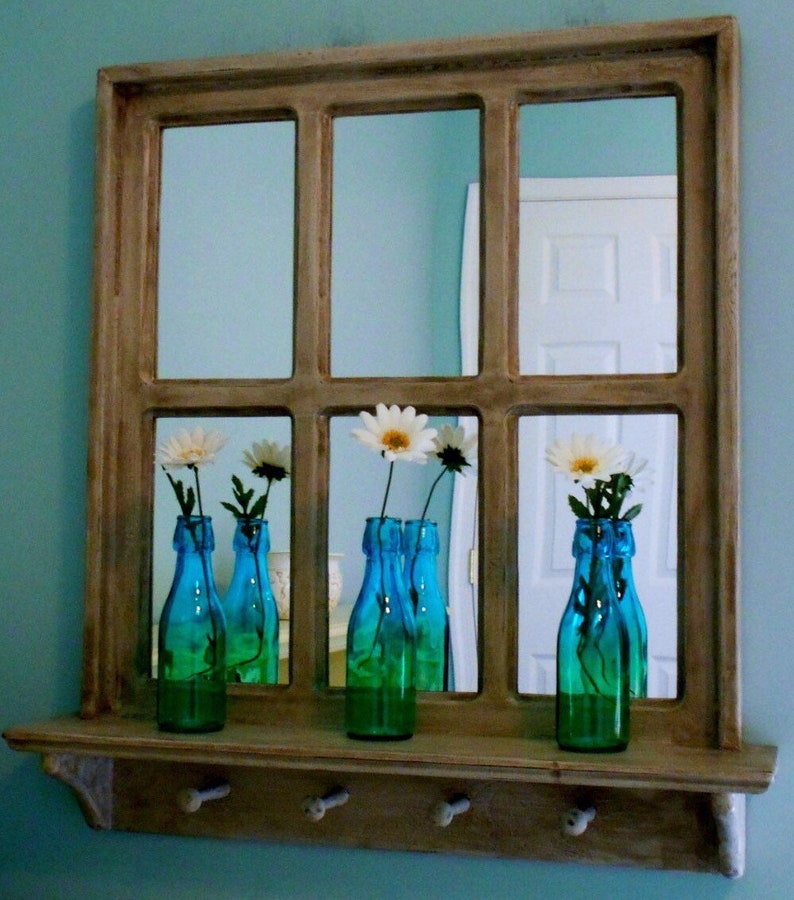 May include: A wooden framed mirror with a shelf and hooks underneath. The mirror is divided into nine panes and reflects white flowers in blue glass bottles.