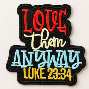 Puede incluir: Un parche bordado negro con el texto LOVE en rojo, them en amarillo claro, ANYWAY en azul claro y LUKE 23:34 en amarillo. El parche tiene un borde negro grueso y una superficie de tela texturizada con costuras de varios colores.