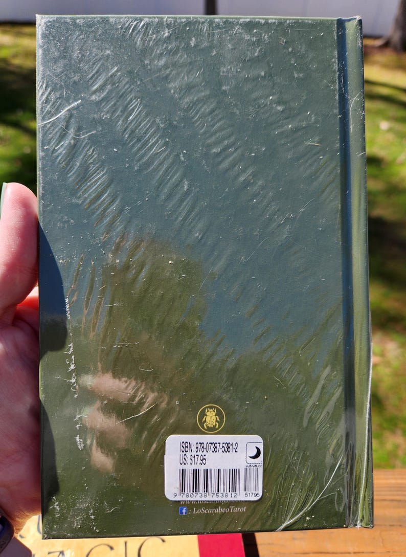 Op de afbeelding: Een groen hardback boek met een sticker op de achterkant. De sticker heeft een barcode, de tekst "ISBN: 978-07387-5381-2", "US $17.95" en een websiteadres. Het boek is verpakt in plastic.