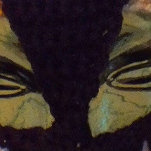 Puede incluir: Primer plano de una m&aacute;scara verde y negra con una superficie texturizada. La m&aacute;scara tiene dos agujeros para los ojos y un dise&ntilde;o cosido.