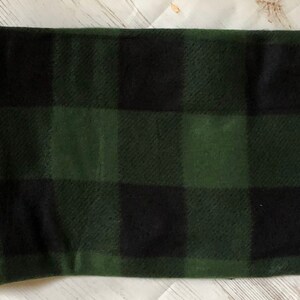 Puede incluir: Una manta doblada con un gran patr&oacute;n de cuadros negros y verdes. La manta tiene un borde cosido. La combinaci&oacute;n de colores recuerda a un tema forestal o al aire libre. La manta est&aacute; hecha de un material suave.