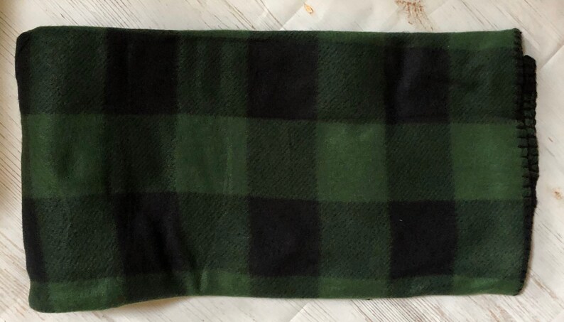 Puede incluir: Una manta doblada con un gran patr&oacute;n de cuadros negros y verdes. La manta tiene un borde cosido. La combinaci&oacute;n de colores recuerda a un tema forestal o al aire libre. La manta est&aacute; hecha de un material suave.