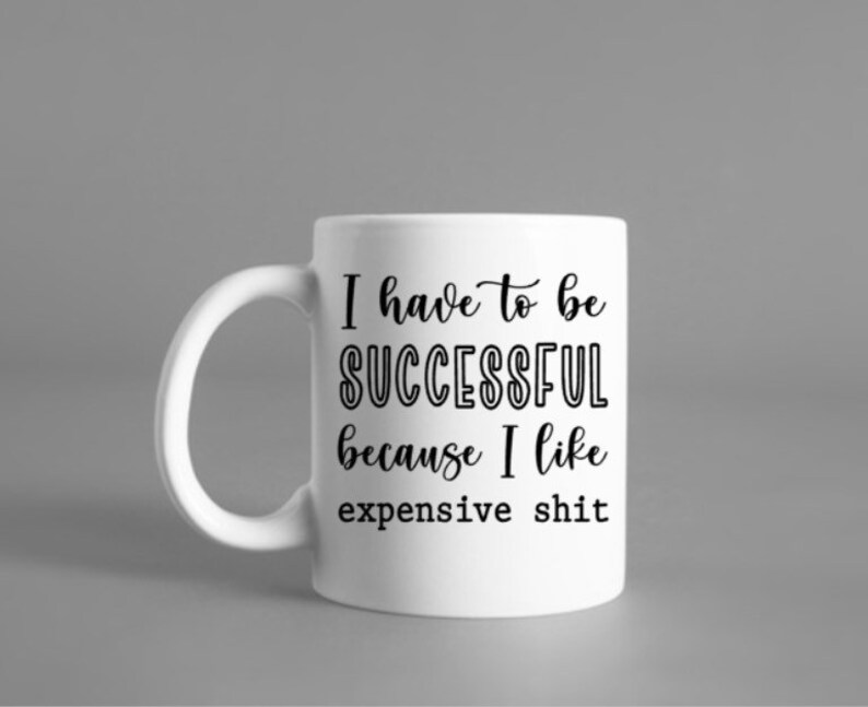 May include: White ceramic mug with a curved handle. The mug features black text that reads "I have to be SUCCESSFUL because I like expensive shit."