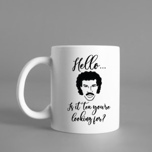 May include: White ceramic mug with a black and white illustration of a man with a mustache and curly hair. The text "Hello... Is it tea you're looking for?" is printed on the mug.