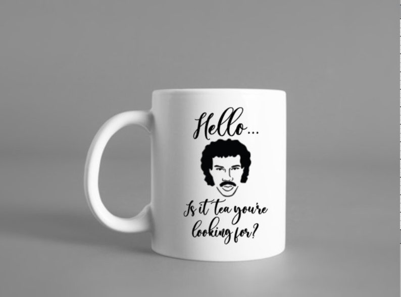 Puede incluir: Taza de cer&aacute;mica blanca con una ilustraci&oacute;n en blanco y negro de un hombre con bigote y pelo rizado. El texto "Hello... Is it tea you're looking for?" est&aacute; impreso en la taza.
