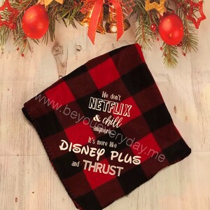 Puede incluir: Manta de forro polar a cuadros rojos y negros con texto blanco. El texto dice: "We don't Netflix & chill anymore... It's more like Disney Plus and Thrust."