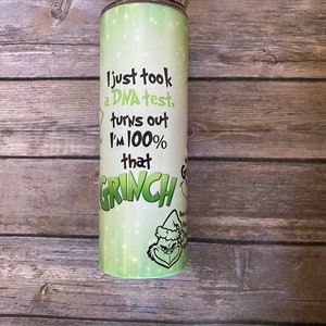 May include: A stainless steel tumbler with a green and white design. The tumbler features the text "I just took a DNA test, turns out I'm 100% that GRINCH" along with a cartoon image of the Grinch.